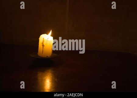 Eine brennende Kerze in einer Kirche gegen die Dunkelheit und einer dunklen Mauer als Symbol für den Glauben, die Religion, das Christentum isoliert Stockfoto