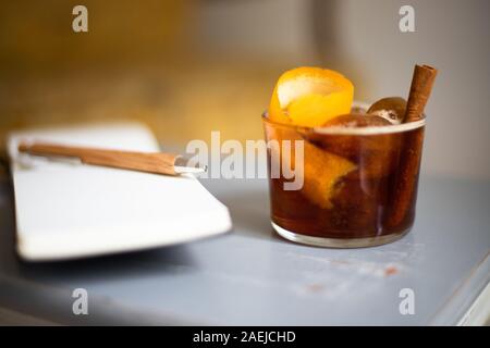 Kalter Kaffee brühen Drink mit Orangenschale und Cinnamon Stick mit Stift und Notizblock auf einem alten Holztisch angeordnet Stockfoto