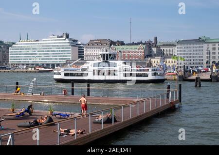 Ansicht von Menschen Sonnenbaden an Allas Meer Pool in der Nähe von South Harbour mit Suomenlinna Fähre und Palace Hotel im Hintergrund, Helsinki, Finnland, Scan Stockfoto