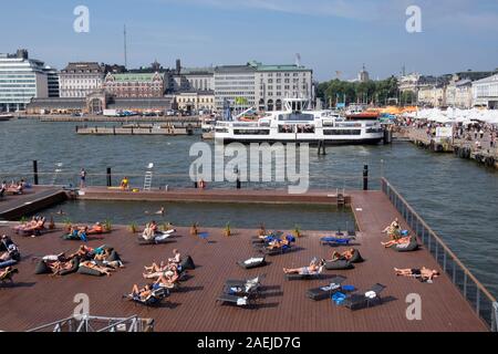 Anzeigen von Menschen Sonnenbaden an Allas Meer Pool in der Nähe von South Harbour mit Suomenlinna Fähre und alte Markthalle Vanha Kauppahalli im Hintergrund erhöht, Er Stockfoto