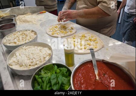 Vorbereitung Pizza Margherita auf einer Marmorplatte. Pizzaiolo stellt Stücke von Mozzarella und Kartoffel über eine rohe Pizza Teig. Stockfoto