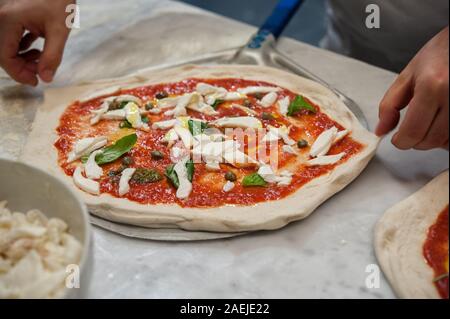 Vorbereitung Pizza Margherita auf einer Marmorplatte. Pizzaiolo setzt Pizza Teig auf die Schale. Selektiver Fokus Stockfoto