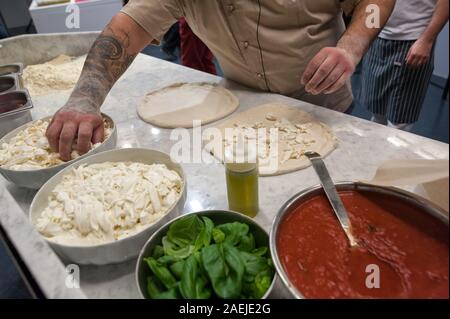 Vorbereitung Pizza Margherita auf einer Marmorplatte. Pizzaiolo stellt Stücke von Mozzarella über eine rohe Pizza Teig. Stockfoto