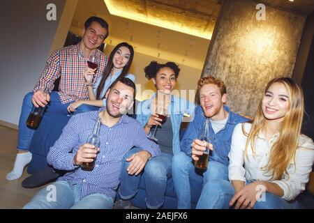 Eine Gruppe von Freunden, die party drinnen Spaß zusammen sitzen auf Trainer trinken Stockfoto