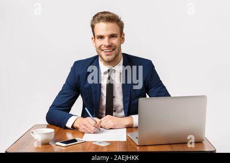 Geschäfts-, Büro- und Unternehmenskonzept. Schöne, freundliche Blonde bärtigen Kerl in klassischen Anzug, Sitzen, Tisch, Schreibtisch mit Laptop, Papiere Stockfoto