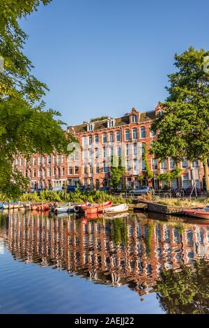 Amsterdam Holland vom 18. Juni 2019 Canal spiegelt die Fassade Gebäude entlang der Seite und die Boote im Wasser schwimmenden an einem hellen Tag mit blauem Himmel ein Stockfoto