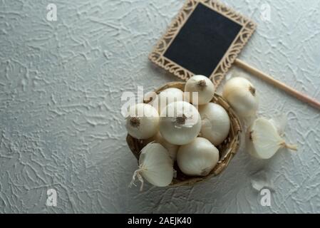 Zwiebeln in eine hölzerne Schüssel mit kleinen schwarzen Brett auf strukturierten Hintergrund. Food Ingredients. Stockfoto