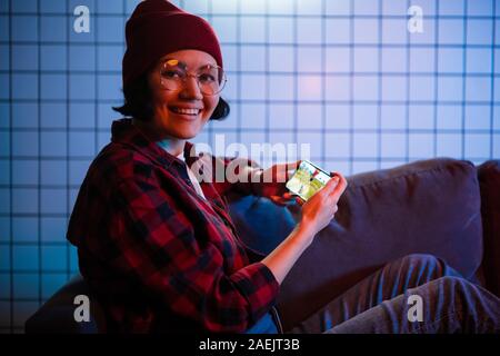 Smart jugendlicher Mädchen sitzt auf einem Sofa zu Hause spielen fps video Spiel auf Ihrem Smartphone, hält und nutzt Handy im horizontalen Modus "Landschaft" Stockfoto