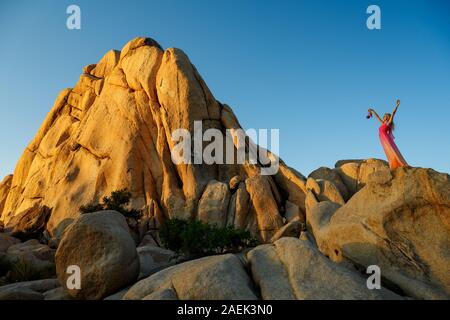 Traum - wie Szene. Elegante Frau, trug einen Fancy Dress, stehend auf einem riesigen Felsen, die Arme in die Luft und halten Sie Ihr High Heel Schuhe. Stockfoto