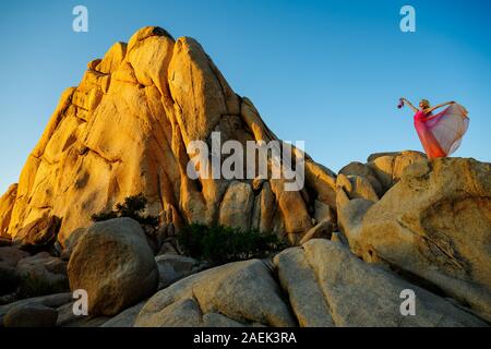 Traum - wie Szene. Elegante Frau, trug einen Fancy Dress, stehend auf einem riesigen Felsen, die Arme in die Luft und halten Sie Ihr High Heel Schuhe. Stockfoto