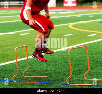 Ein High School Football Player über orange Hürden während der Saison einen Sprung auf ein grüner Rasen. Stockfoto