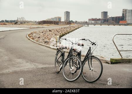 Zwei identische Retro schwarz Stadt Fahrräder am Bahndamm entlang der Straße geparkt, Ostsee, bahndamm mit Asphalt weg Hintergrund der Sdan und Stadt Stockfoto