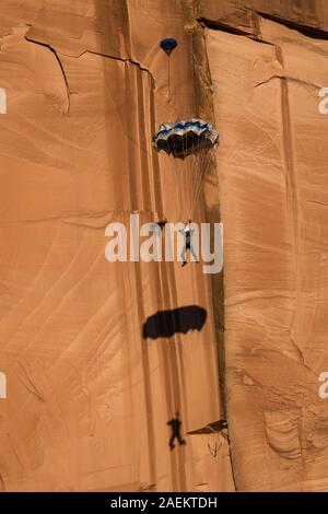 Ein Base Jumper fällt in seinem Fallschirm aus der 400-Fuß vertikale Teilfläche der Tombstone in der Kane Springs Canyon in der Nähe von Moab, Utah. Hinweis sein Schatten auf Th Stockfoto