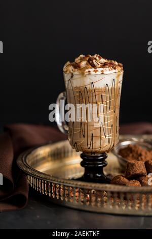 Eine Nahaufnahme eines dekorativen Glas Tasse heißen Cappuccino mit Sahne, gehackte Pekannüsse und Kakao besprüht und mit Schokolade truff serviert. Stockfoto