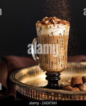 Nahaufnahme eines Caramel heißen Getränk mit Sahne und Kakao bestreut sein Auf und serviert mit Schokolade Trüffel. Stockfoto