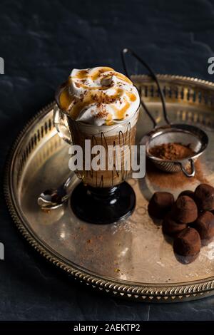 Eine Top-down-Sicht auf ein dekoratives Glas heißen Cappuccino und Sahne und garniert mit Kakao bestreut und serviert mit Trüffeln. Stockfoto