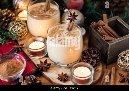 Aus der Nähe zu sehen. Zwei Gläser Eierpunsch mit Zimt und Sternanis und von Weihnachtsschmuck und Kerzen umgeben. Stockfoto