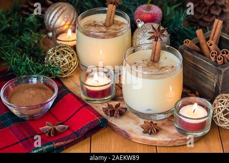 Aus der Nähe zu sehen. Zwei Gläser voll von eierpunsch mit Zimt auf bestreut und mit Zimt und Weihnachtsschmuck umgeben. Stockfoto