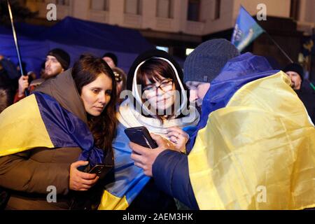Kiew, Ukraine. 10 Dez, 2019. Die ukrainer auf einem Smartphone Nachrichten über die Normandie vier Leaders Summit, Volodymyr Zelensky, Wladimir Putin, Merkel und Emmanuel Längestrich außerhalb des Präsidialbüros in Kiew. Ein Normandie Format Gipfel mit der Teilnahme von Verantwortlichen der Ukraine, Russland, Frankreich und Deutschland hinsichtlich der Konflikte in der östlichen Ukraine in Paris stattfand. Credit: SOPA Images Limited/Alamy leben Nachrichten Stockfoto