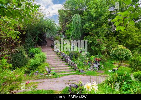 Eine lange, hohe Treppe mit Holzstufen Verlängerung nach oben durch Steine und grünen Pflanzen im Sommer im Garten umgeben. Reisen und mystische Orte. Stockfoto