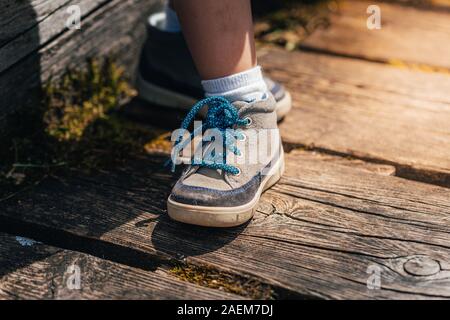 Blau und Grau Wandern Schuh von einem jungen Kind auf einem Holzbrett von einer Brücke in den Alpen in Deutschland mit der Sonne im Sommer.