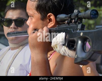 Hingerissen Thai Chinesische taoistische Anhänger durchdringt seine linke Wange mit einem Gewehr barrel während der Phuket Vegetarian Festival (neun Kaiser Götter Festival). Stockfoto