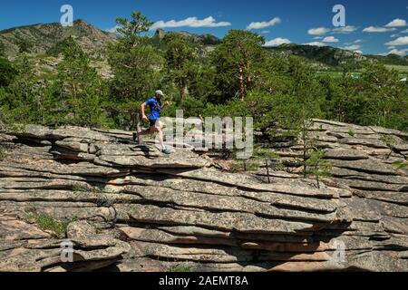 Der Athlet läuft auf die Felsen in den Bergen. Outdoor Trail Running. Mann im blauen T-Shirt und schwarze Shorts training Stockfoto
