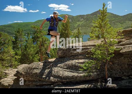 Runner Klettern ein Fels. Der Athlet läuft auf die Felsen in den Bergen. Outdoor Trail im sonnigen Tag läuft. Mann im blauen T-Shirt und schwarze Shorts Zug Stockfoto