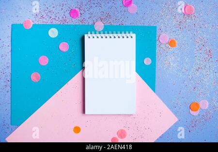 Flach mit Notizblock und Bleistift auf bunten Hintergrund mit Glitter und Konfetti. Vorsätze im Neuen Jahr Konzept. Stockfoto