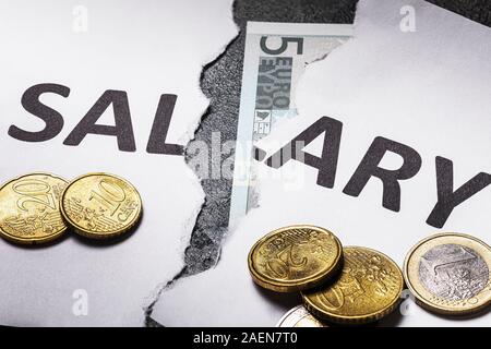 Ein weißes Blatt Papier mit den Worten Gehalt in der Hälfte mit Euro-münzen zerrissen auf dem Tisch Stockfoto
