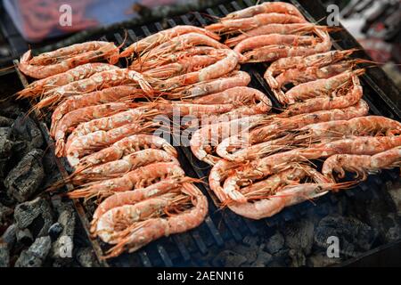 Kochen große und frische Garnelen auf dem Grill, die auf den Kohlen liegt. Langustinen liegen auf dem Grill. Stockfoto