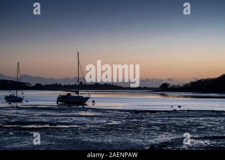 Sonnenuntergang bei Dell Kai Sailing Club in der Nähe von Chichester. Sonne hinter zwei Yachten in einer Farbenpracht und Reflektieren von Wasser und Sand bei Ebbe Stockfoto