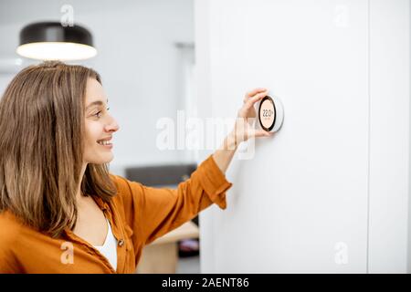 Junge Frau, die Regelung der Heizung Temperatur mit einem modernen drahtlosen Thermostat auf der weißen Wand zu Hause installiert. Smart Home Heizung Verordnung Konzept Stockfoto