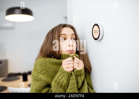 Junge Frau in Pullover frieren, Warten auf das Haus zu erwärmen, Steuerung Heizung mit einer smart home Thermostat Stockfoto