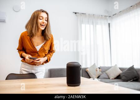Junge fröhliche Frau controlling home Geräte mit einem Sprachbefehle, um eine Smart Spalte zu Hause sprechen. Konzept der "Smart Home" und Sprachsteuerung Stockfoto