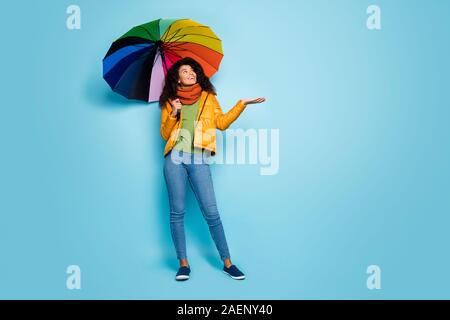 Volle Länge Foto des schönen dunklen Haut Dame halten bunte Dach fallenden Regentropfen tolles Wetter tragen Mantel jeans Grünen pullover schal genießen Stockfoto