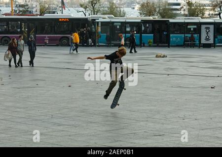 Junge stilvolle Skateboarder tut ein Sprung Trick, während seine Arme weit offen an einem bewölkten Tag im öffentlichen skateboard Park in Besiktas. Stockfoto