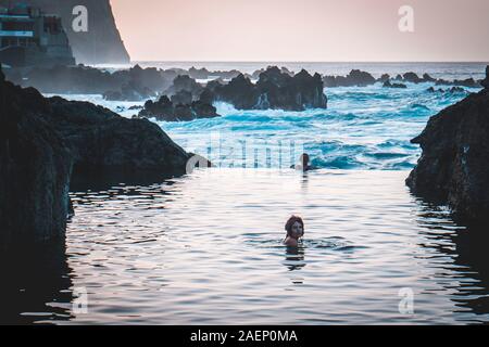 Portugal, Madeira: junge frau Schwimmen in einem natürlichen Meerwasserschwimmbecken von Felsen umgeben, in Porto Moniz, mit dem Meer im Hintergrund Stockfoto