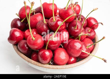 Ein Bündel von frischen roten Kirschen angeordnet und in kleine runde Steinzeug Schüssel auf weißem Hintergrund. Stockfoto
