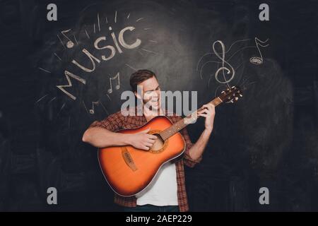 Junge glücklich Mann spielen an der Gitarre und singin vor dem Hintergrund des Schwarzen Brettes Stockfoto