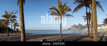 Breites Panorama aus dem Arpoador Boulevard mit den Sonnenaufgang über den Strand von Ipanema in Rio de Janeiro mit Palmen im Vordergrund. Stockfoto