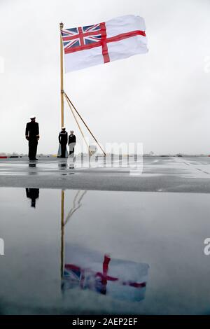 Mitgliedern der Besatzung heben die weiße Fahne auf dem Stern der Royal Navy Flugzeugträger HMS Prince of Wales, während ihrer Inbetriebnahme Zeremonie an der Portsmouth Naval Base. Stockfoto