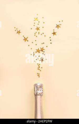 Champagner Flasche mit Konfetti Sterne auf goldenen festlichen Hintergrund. Weihnachten, Geburtstag oder Hochzeit Feier Konzept. Flach, kopieren. Stockfoto