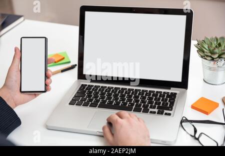 Handy und Laptop mit weißen leeren Bildschirme, Mann bei der Arbeit in seinem Büro Schreibtisch, geschäftlichen Hintergrund, kopieren. Stockfoto