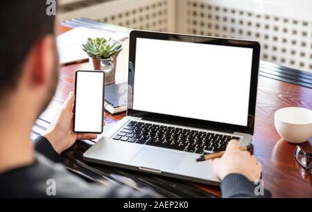 Handy und Laptop mit weißen leeren Bildschirme, Mann bei der Arbeit in seinem Büro Schreibtisch, geschäftlichen Hintergrund, kopieren. Stockfoto