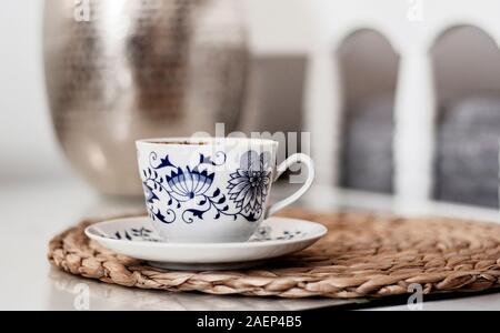 Tasse Kaffee auf korbstühlen stehen auf einem weißen Tisch Glas, Metall Vase auf dem Hintergrund, gemütliches Heim Innenraumkonzept Stockfoto