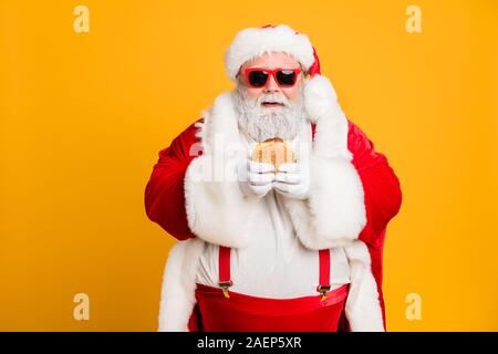 Portrait von Lustige funky fat Santa Claus nicht für Gesundheit fast food big Sandwich auf x-mas Tradition Feier tragen Stil stilvolle Hosenträger Essen Stockfoto
