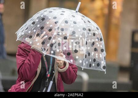 Frau am Handy unter dem Regenschirm an einem regnerischen Tag in Southport, Lancashire. UK Wetter; UK 10. Dezember 2019 Wetterwarnungen für starken Regen und starken Wind an der Westküste. Quelle: MediaWorldImages/AlamyLiveNews Stockfoto