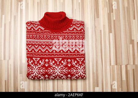 Rot gestrickt Weihnachten rollkragen pullover oder Pullover aus traditionellem Design mit weißen Skandinavischen geometrische Verzierung auf hölzernen Hintergrund gelegt gefaltet Stockfoto