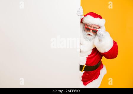 Portrait von Lustige funky santa claus Rot headwear Blick hinter weißen Billboard Wunder unglaubliche 2020 Weihnachtszauber Advent elegante schwarze Riemen auf Verschleiß Stockfoto